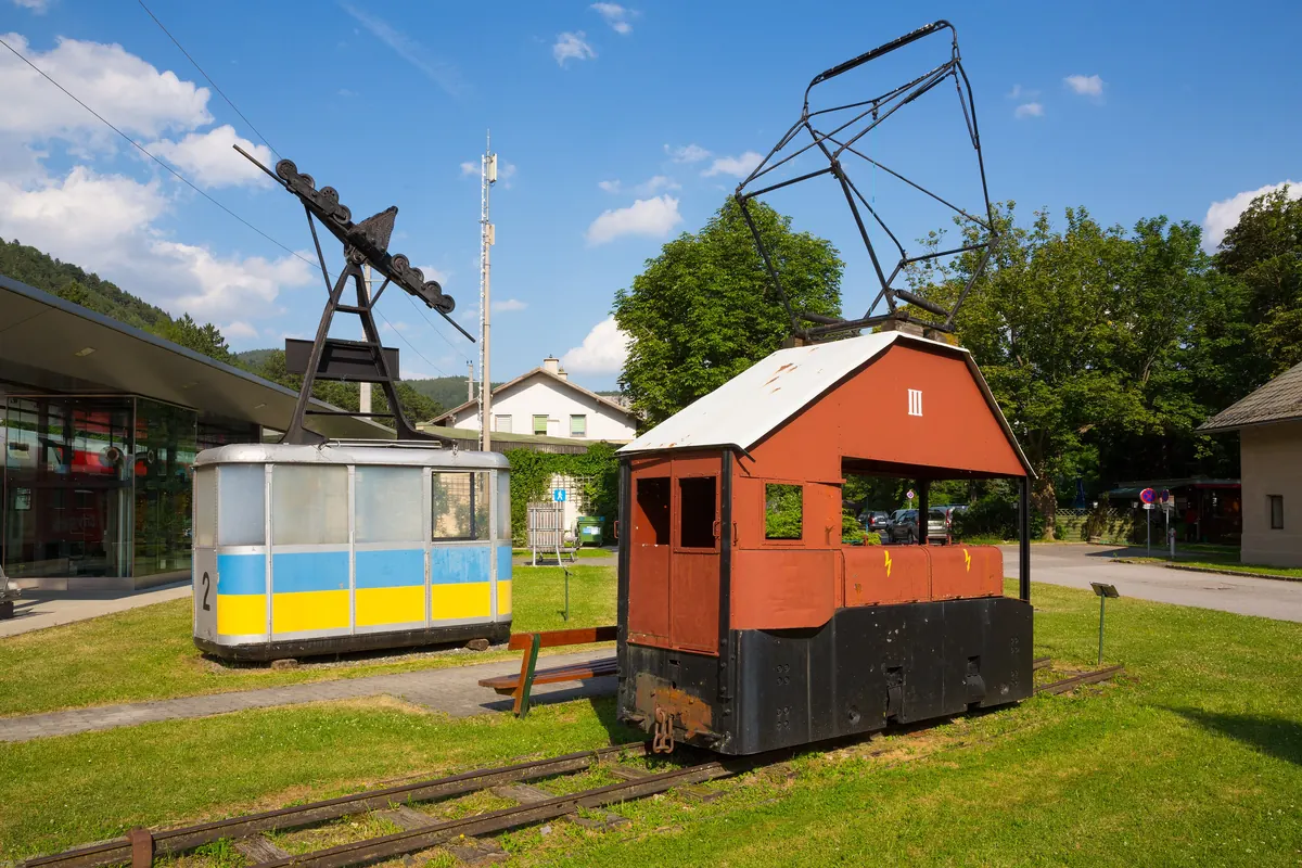 Two old cabins of the Raxseilbahn, one blue and yellow, one of red wood, standing on the lawn at Payerbach station.