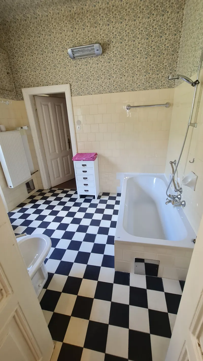 A bathroom with a black and white checkered floor, a deep white bath and patterned wallpaper.