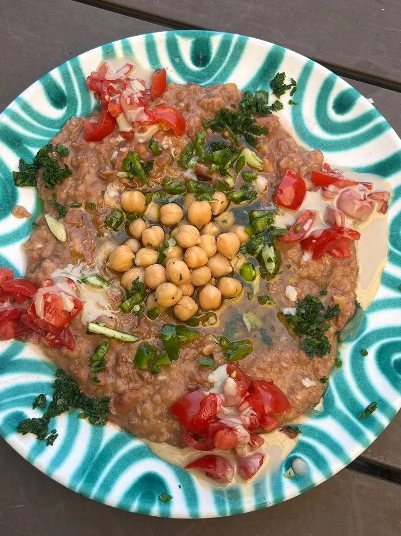 Fatteh topped with tomatoes, chickpeas and green chilli on a green and white plate.