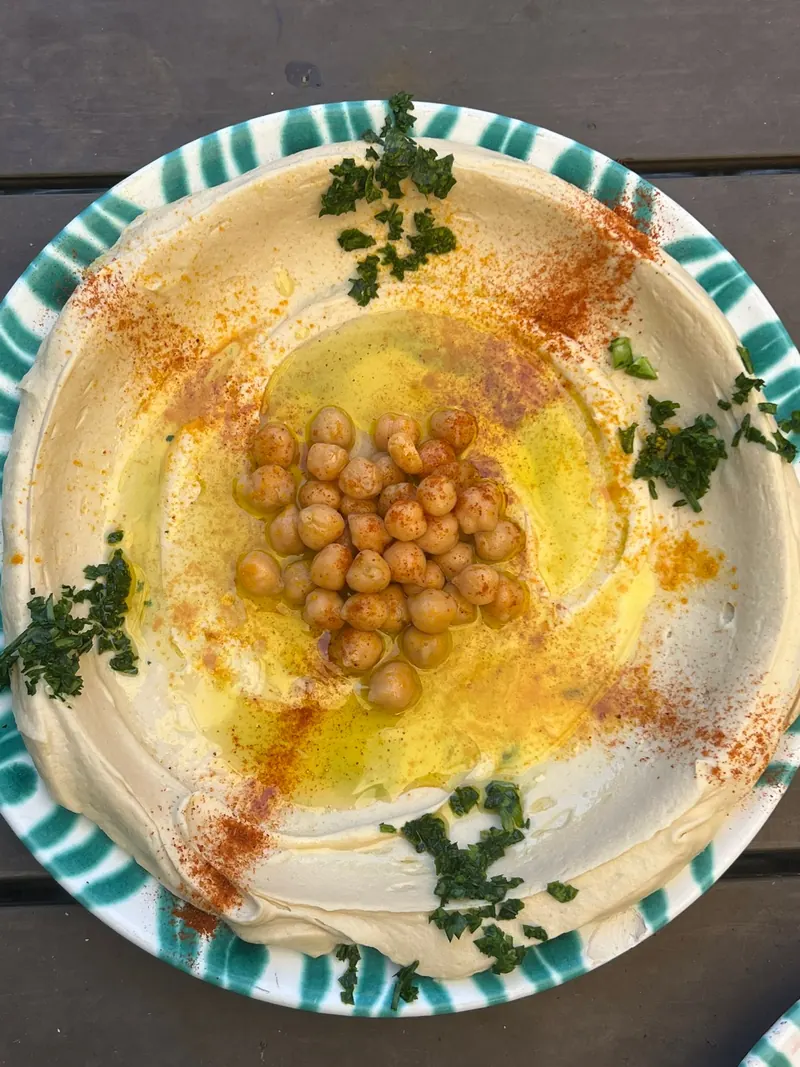 Hummus with olive oil, paprika, chickpeas and parsley on a green and white Gmundner plate.