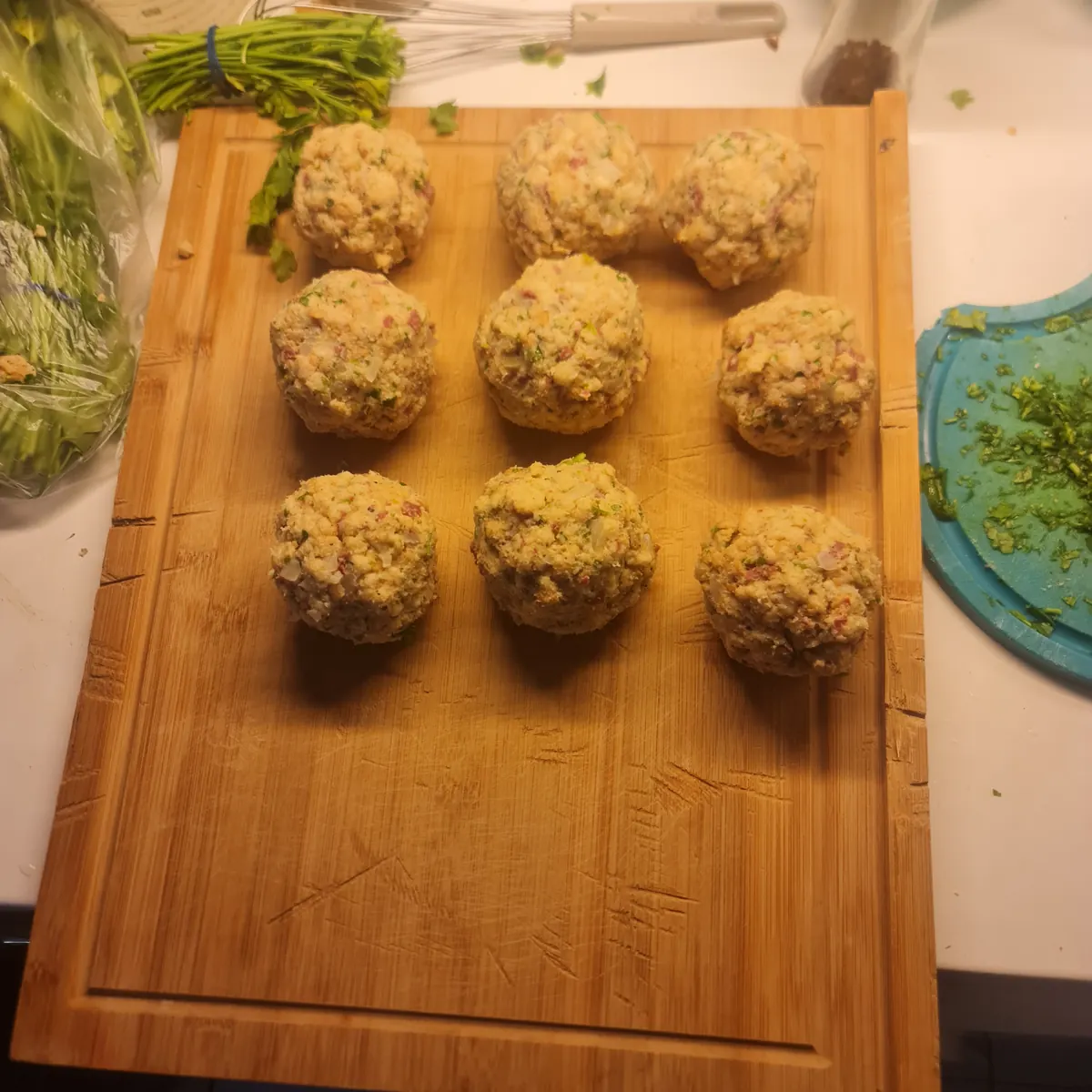 Nine Knödel on a wooden cutting board, rolled and ready to cook.