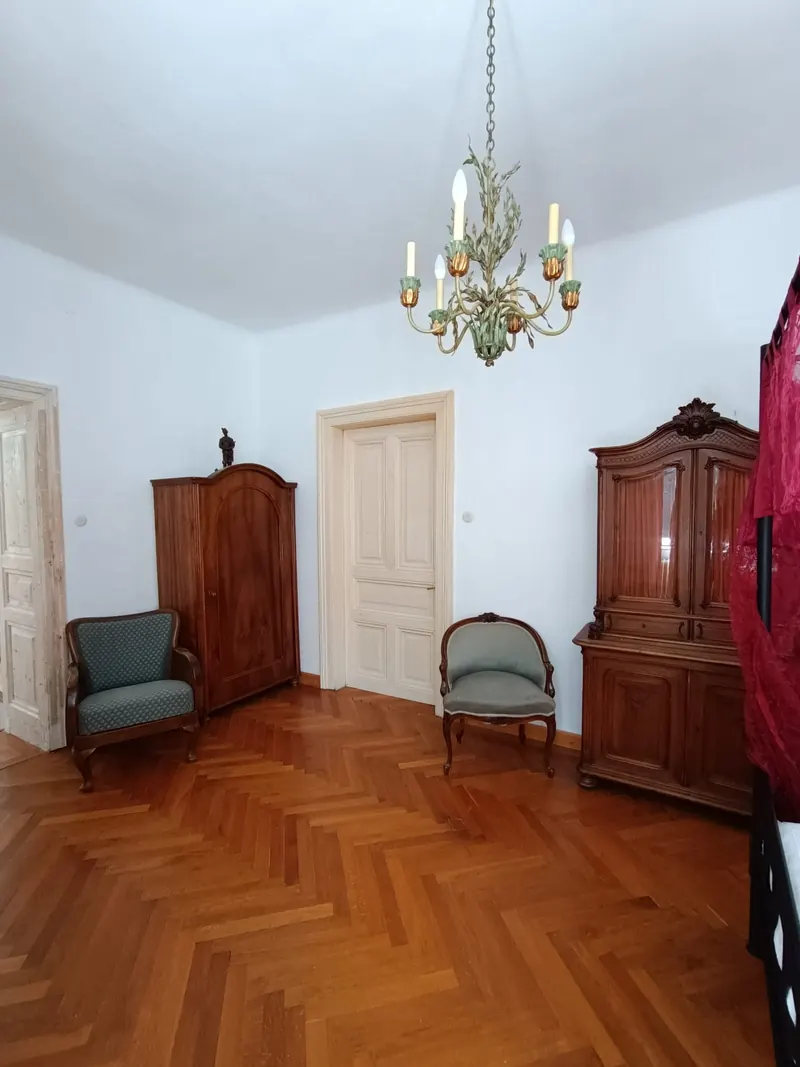 A tall room with a chandelier, two wooden wardrobes, two armchairs and a panelled double door.